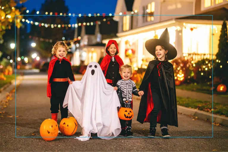 Kids in their Halloween costumes walking in the street during early evening.