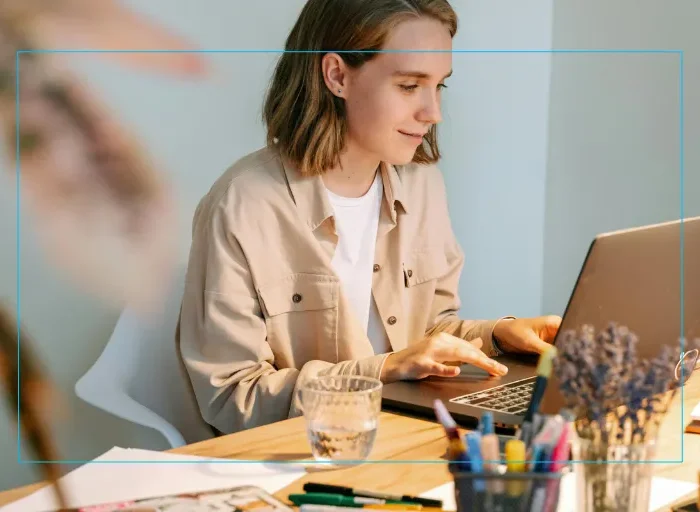 A young woman typing on her laptop wearing a tan denim jacket