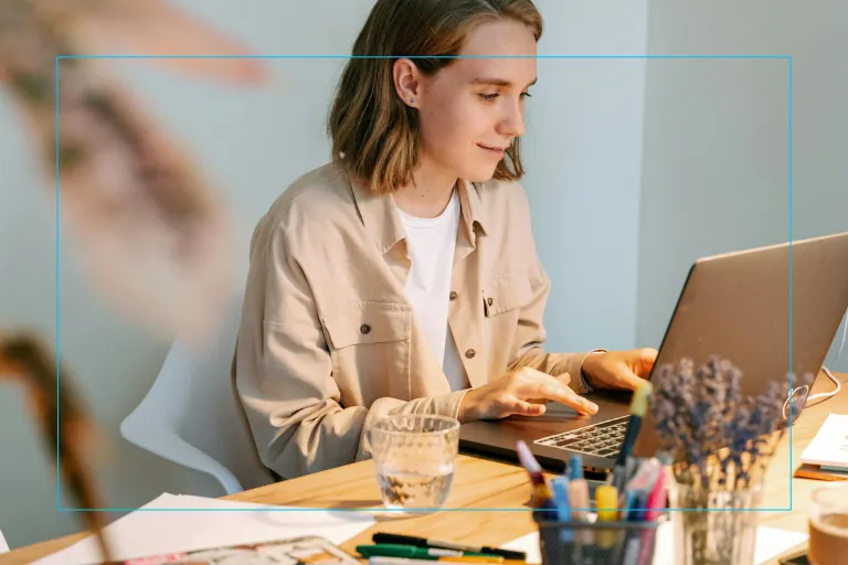 A young woman typing on her laptop wearing a tan denim jacket