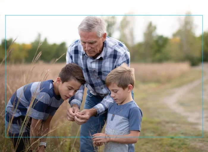 An older man with his 2 grandsons in a wooded area.