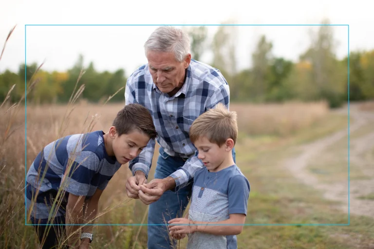 An older man with his 2 grandsons in a wooded area.