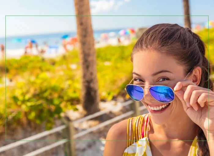 Smiling girl beachside on a sunny day pulling down her glasses.
