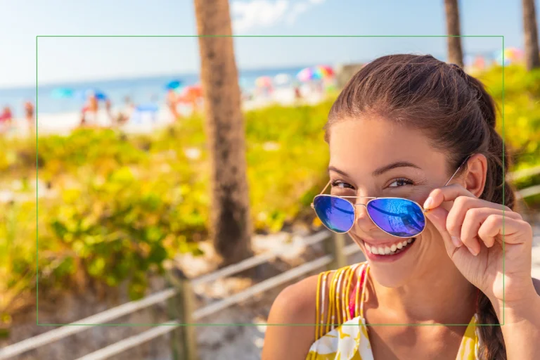 Smiling girl beachside on a sunny day pulling down her glasses.