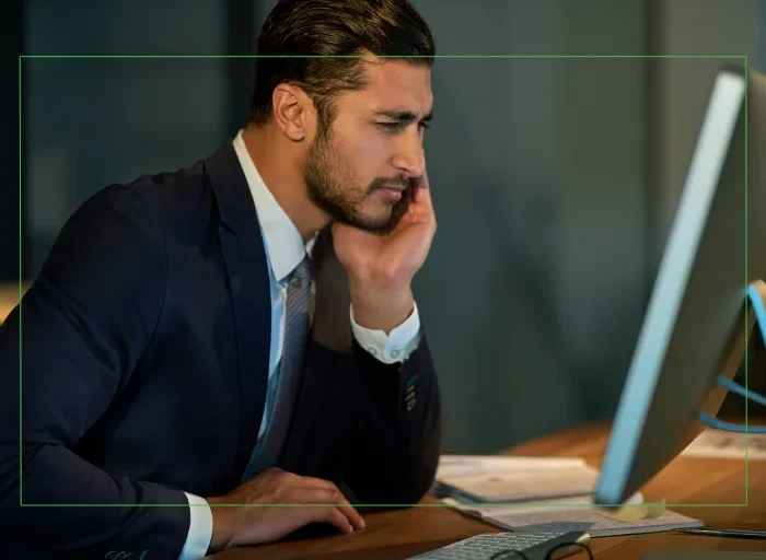 Business professional in a suit leaning on his hand while staring at a computer screen, suggesting eye strain or fatigue from prolonged screen use