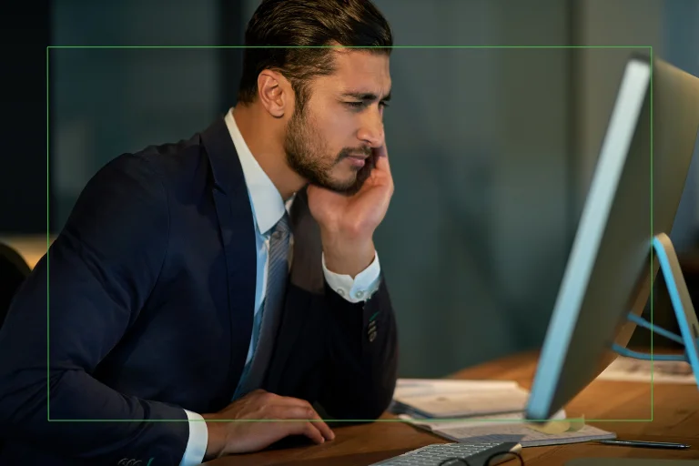 Business professional in a suit leaning on his hand while staring at a computer screen, suggesting eye strain or fatigue from prolonged screen use