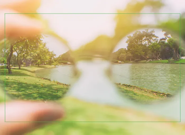Person looking through eyeglasses at a clear outdoor scene, representing a mid-year vision reset and the transition from glasses to LASIK or lens replacement surgery.
