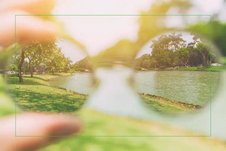 Person looking through eyeglasses at a clear outdoor scene, representing a mid-year vision reset and the transition from glasses to LASIK or lens replacement surgery.